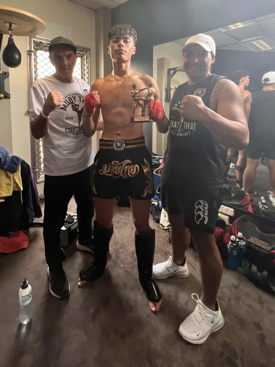 A Stormforce fighter holding a trophy with two coaches after a bout